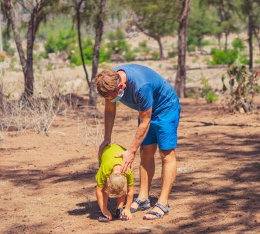 Spor baba oğul ormanda temiz hava alıyor, birlikte antrenman yapıyor, çömelme ve yan bükme tekniği uyguluyor, maske takıyor, Coronavirus yürüyüş doğa güneşini koruyor. Baba oğlanı etkiler.