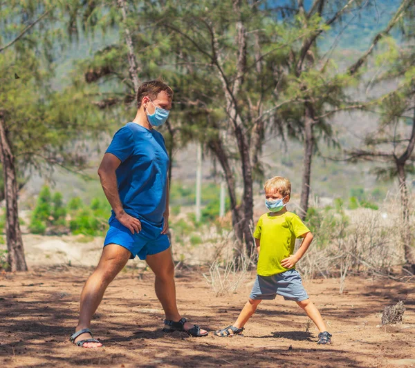 Sport father son exercising in forest park fresh air, workout enjoying together, squatting and side bend technique, wear face blue mask protect coronavirus walk nature sun day. Daddy influence on boy
