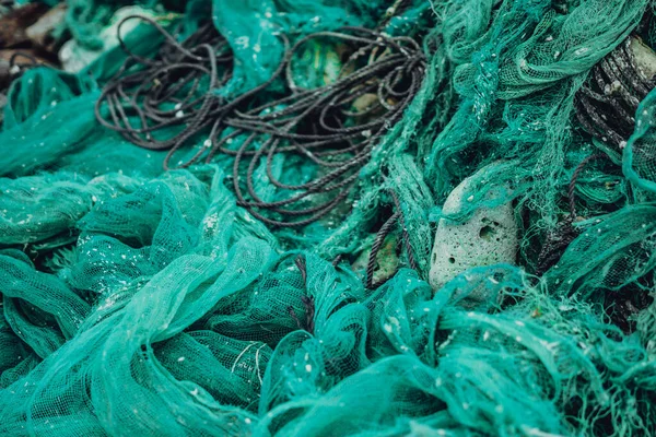 Close up view pile of green nylon multi colorful bright fish nets with pieces of white corals and old ropes in fishing village. Still life background pattern. Hobby fishing concept. Copy space