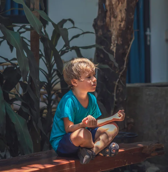 Tranquilo niño varón siéntate en el sofá fuera de la práctica de yoga jardín. El descanso infantil moderno de la generación joven alivia las emociones negativas con los ojos cerrados en la pose de loto al amanecer. Concepto de meditación Mindfulness —  Fotos de Stock