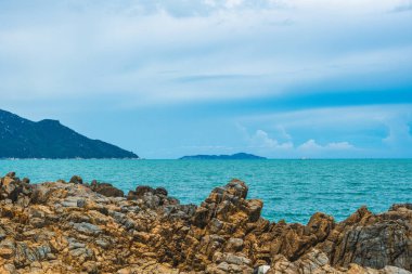 Güzellik panorama canlı kahverengi kaya eski püskü uçurum, saf mavi tembel denizde ufuk çizgisi, kümülüs bulutu gökyüzü, dağ adası arka planı, boş deniz arka planı. Yaz tatilinden sonra turizm eğlencesi