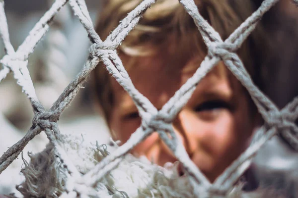 Blond blur little boy hide look behind knitting mesh net. Soft focus. Bad unhappy ignore offended mood. Problem childhood, child relationships psychology problem, harassment physical abuse concept — Stock Photo, Image