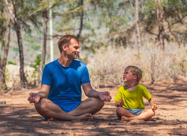 Father meditates yoga pose in forest park on fresh air, son repeats, smiling happy look at each other. Daddy influence on boy worldview. Fatherhood relationship. Children imitate behavior Childhood — Stock Photo, Image