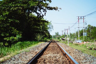 Demir raylar ileri, çakıllar, ufukta güneş gökyüzü ağacı, elektrik direkleri, banliyö binaları manzarası. Demiryolu turizmi, ulaşım endüstrisi yaz günü konsepti