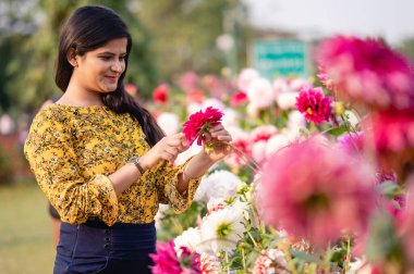 Güzel bir genç kız renkli çiçeklerin bitkisiyle birlikte duruyor. Sarı elbiseli, siyah saçlı bir kız. Portre. Aşk..