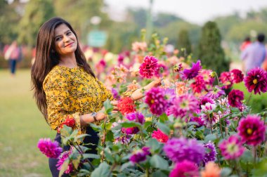 Güzel bir genç kız renkli çiçeklerin bitkisiyle birlikte duruyor. Sarı elbiseli, siyah saçlı bir kız. Portre. Aşk..