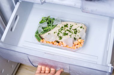 Buzdolabında dondurulmuş sebzeler ve balıklarla dolu bir kap. Donmuş hazır yemek kavramı ve yemek pişirmek zaman kazandırıyor..