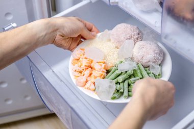 Kadın elleri buzdolabındaki dondurucudan bir tabak donmuş yiyecek alıyor. Hazır yemek depolama kavramı zaman kazandırıyor..