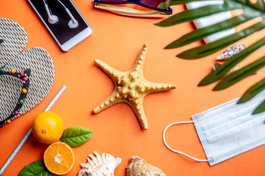 Turuncu arka planda deniz yıldızı etrafında plaj tatili için aksesuarlar. Bir salgın sırasında denize seyahat ve tatil kavramı. Üst görünüm