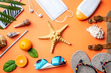 Turuncu arka planda deniz yıldızı etrafında plaj tatili için aksesuarlar. Bir salgın sırasında denize seyahat ve tatil kavramı. Üst görünüm