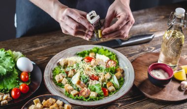 Şef peyniri iştah açıcı taze bir salata olarak rendeliyor. Lezzetli yemek yapma kavramı Sezar