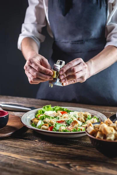 Şef peyniri iştah açıcı taze bir salata olarak rendeliyor. Lezzetli yemek yapma kavramı Sezar