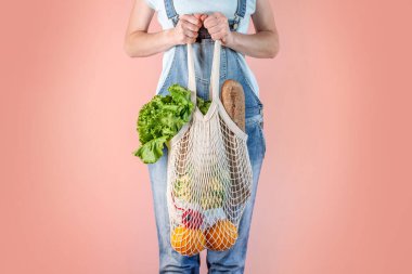 Kot pantolon giymiş modern bir kadın elinde bir torba dolusu mal tutuyor. Çevre dostu davranış anlayışı, yeniden kullanılabilir çantaların kullanımı ve çevre kaygısı