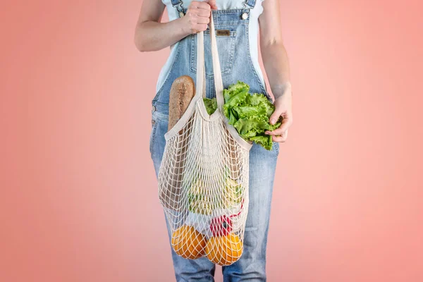 A modern woman in jeans is holding a string bag with purchases. Concept of eco-friendly behavior, the use of reusable bags and concern for the environment