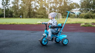 Küçük bir çocuk başarılı bir şekilde üç tekerlekli bisiklete biner. Bisiklet sürmeyi öğrenme ve aktif zaman geçirme kavramı.