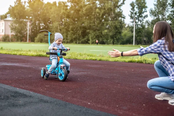 Mutlu küçük çocuk başarılı bir şekilde üç tekerlekli bisikletle annesine gidiyor. Bisiklet sürmeyi öğrenme ve ailenle eğlenme kavramı..