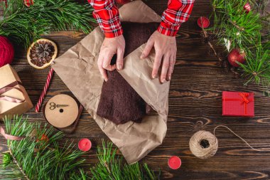 Kadın, içinde kazak olan dikiş kağıdının ilk kenarını sarıyordu. Noel hediye paketleme sürecinin ikinci adımı.