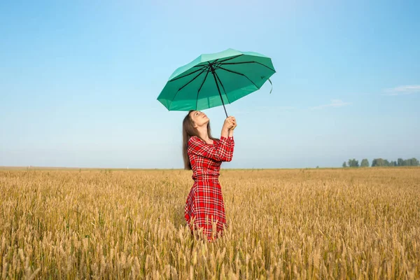 一个穿着红色衣服 拿着绿色雨伞的年轻女子 她站在麦田里的金色小穗中间 安宁和自由的概念 — 图库照片