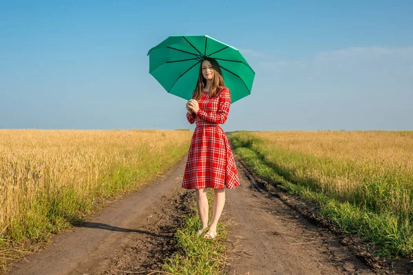 一个身穿红色衣服 头戴绿色雨伞的年轻女子正沿着麦田的大路走着 安宁和自由的概念 — 图库照片