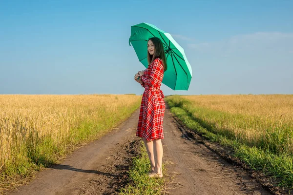 一个身穿红色衣服 头戴绿色雨伞的年轻女子正沿着麦田的大路走着 安宁和自由的概念 — 图库照片