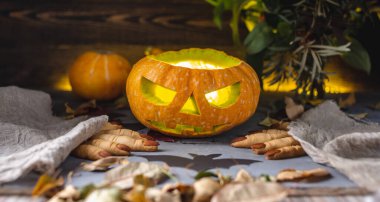 İçinde ışık ve yüzü olan bir balkabağı ve cadılar bayramı partisi için bir cadının parmaklarını kurabiyeler. Tatilin kötü atmosferi kavramı.