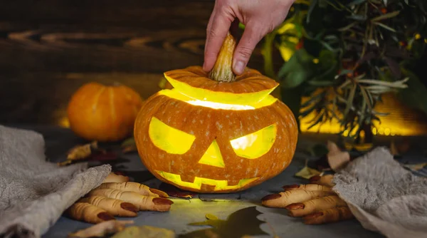 Hand is opening the pumpkin with the face cut out. Concept of celebrating Halloween and a magical mysterious and scary atmosphere.