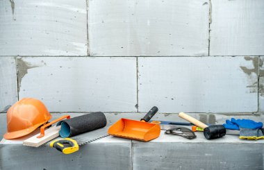 İnşaat alanındaki havalandırmalı beton bloklardan oluşan bir duvarın arka planında inşaat aletleri var..