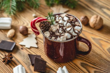 Noel aksesuarlarıyla çevrili ahşap bir masada kırmızı şekerle süslenmiş bir fincan aromalı sıcak çikolata. Neşeli bir atmosfer ve rahat bir yeni yıl havası..