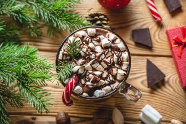 Noel aksesuarlarıyla çevrili ahşap bir masada kırmızı şekerle süslenmiş bir fincan aromalı sıcak çikolata. Neşeli bir atmosfer ve rahat bir yeni yıl havası..
