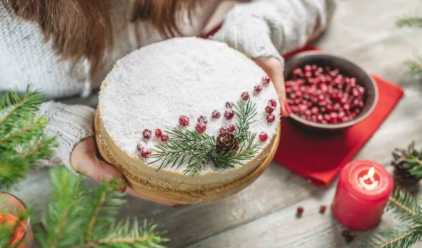 女性は雪を模したココナッツフレークで覆われ 赤い果実 コーン モミの枝で飾られたお祝いの白いムースケーキを開催しています 新年とクリスマスの概念 — ストック写真