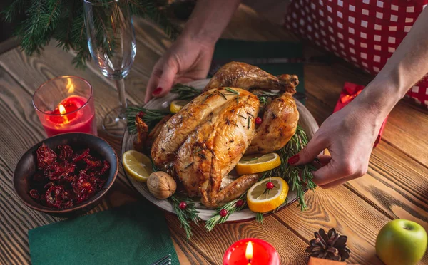 Hands are holding a dish of baked chicken with rosemary and berries on a wooden table. Traditional Christmas dish for a festive dinner in a rustic style