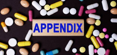 APPENDIX kelimesi, çok renkli hapların yanındaki karanlık bir masada, tahta bir bloğa yazılmıştır. Tıbbi konsept