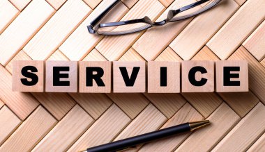 SERVICE kelimesi, siyah çerçeveli gözlük ve kalemin yanındaki tahta bloklara yazılmıştır. İş konsepti