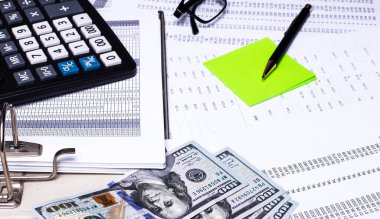 Raporlarda bir hesap makinesi, para, yeşil bir çıkartma ve bir kalem var. İş konsepti