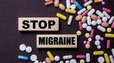 DUR MIGRAINE, karanlık bir arka planda hapların arasında tahta bloklara yazılmıştır. Tıbbi konsept