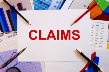 CLAIMS kelimesi grafikler, kalemler ve kalemlerin yanındaki beyaz bir kağıt parçasına kırmızı ile yazılmıştır. İş konsepti