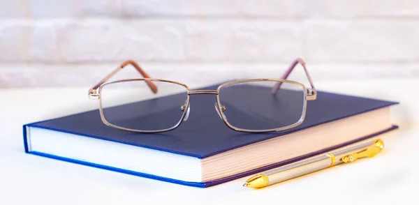 Gold-rimmed glasses lie on a blue diary. Near the handle. Workplace close up