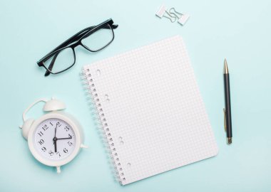 Mavi arka planda beyaz bir defter, beyaz ataç, siyah gözlük ve bir kalem var. Düz yatıyordu. Boşluğu kopyala