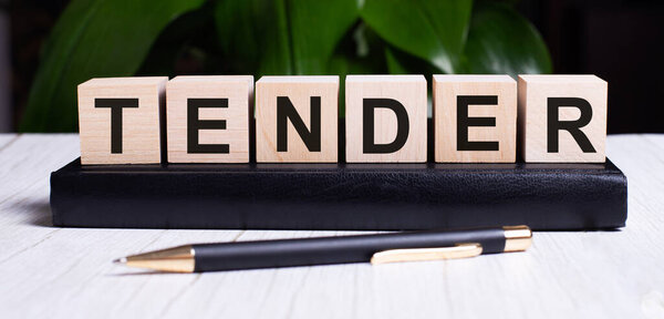 TENDER написан на деревянных кубиках возле ручки и блокнота. Концепция бизнеса