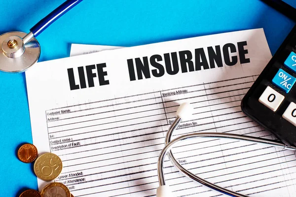 LIFE INSURANCE is written on the insurance policy next to the stethoscope, calculator and coins. Medical and insurance concept