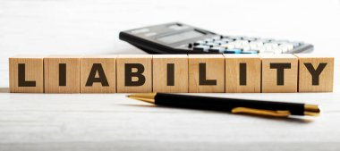 LIABILITY kelimesi, hesap makinesi ile kalem arasındaki tahta kesiklerin üzerine hafif arkaplanda yazılır..