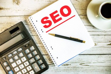 SEO kelimesi, hesap makinesi ile açık tahta bir masanın üzerindeki bir fincan kahve arasında günlük bir günlüğe yazılmıştır. İş konsepti
