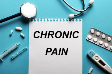 Mavi arka planda steteskop, haplar, şırıngalar yazılı kronik ağrısı olan bir kağıt parçası var. Tıbbi konsept