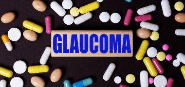 Koyu bir arka planda, çok renkli haplar ve tahta bir blokta GLauKOMA kelimesi. Tıbbi konsept