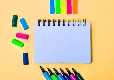 Bej bir arka planda, boş bir defter, parlak kalemler ve çıkartmalar. Boşluğu kopyala