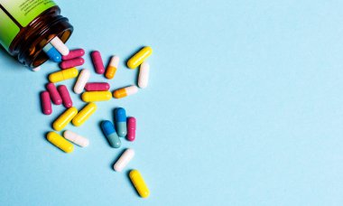 Çok renkli kapsüller mavi arka planda bir şişeden yayılmış.