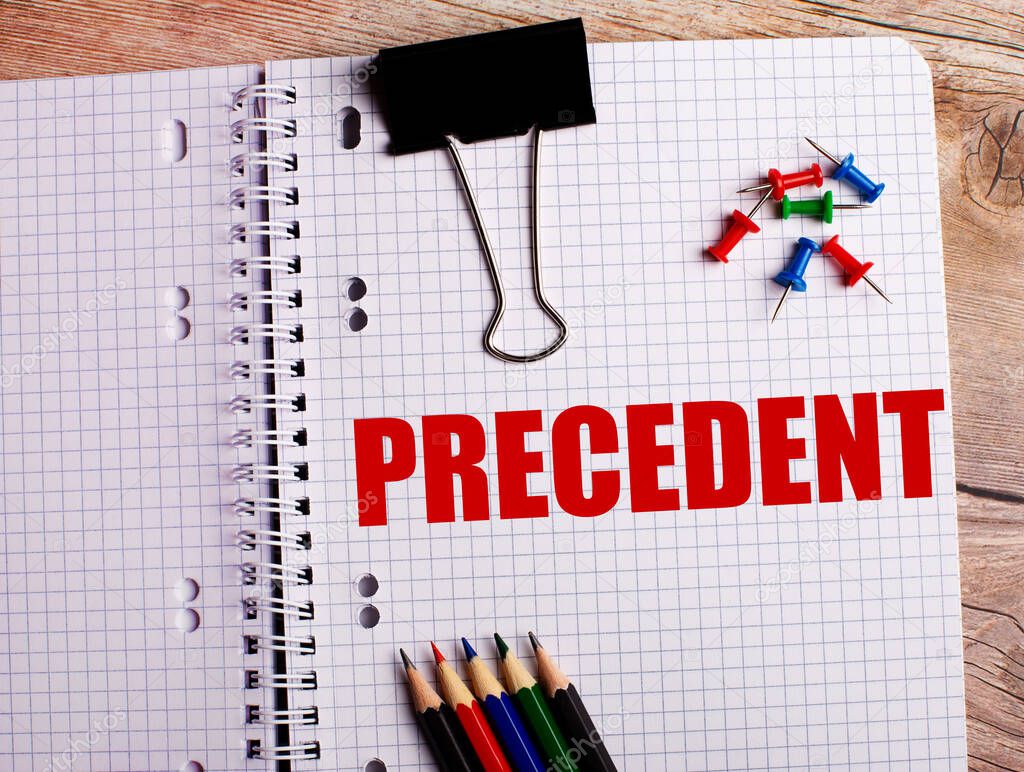 The word PRECEDENT is written in a notebook near multi-colored pencils and buttons on a wooden background.