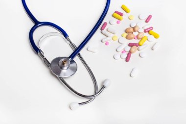 Stetoskop ve çok renkli haplar arka planda yatar. Tıbbi konsept