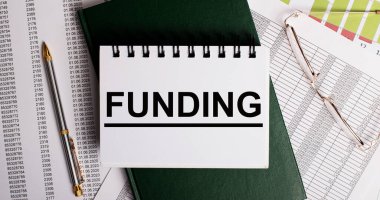 Masaüstünde raporlar, gözlükler, bir kalem, yeşil bir günlük ve üzerinde 