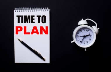 Time to Plan siyah zemin üzerinde beyaz bir çalar saatin yanında beyaz bir not defterine yazılır..